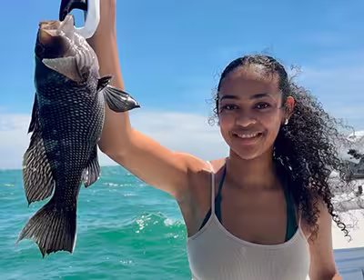 Book a nearshore fishing charter in Ocean Isle Beach today! Female angler holding a keeper Sea Bass caught nearshore from Ocean Isle Beach NC