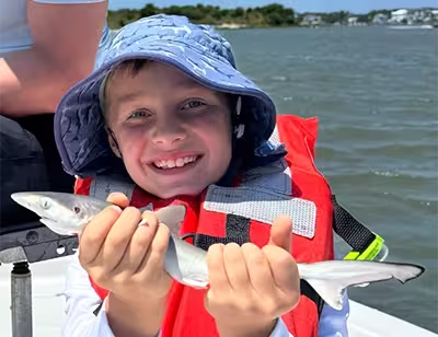 Shark caught during an inshore kids fishing charter in Ocean Isle Beach, NC Kid holding a small shark caught on a kids fishing trip in Ocean Isle Beach, NC